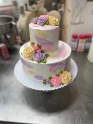 Two tier cake with pink, purple and yellow flowers and decorations